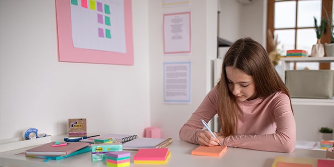 Student making notes on Post-it® Notes in a study space with various stationery items, including Post-it® Notes and notebooks
