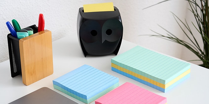 A desk with Post-it® Notes in various colours, a pen holder, and a black owl-shaped Post-it® Note Dispenser
