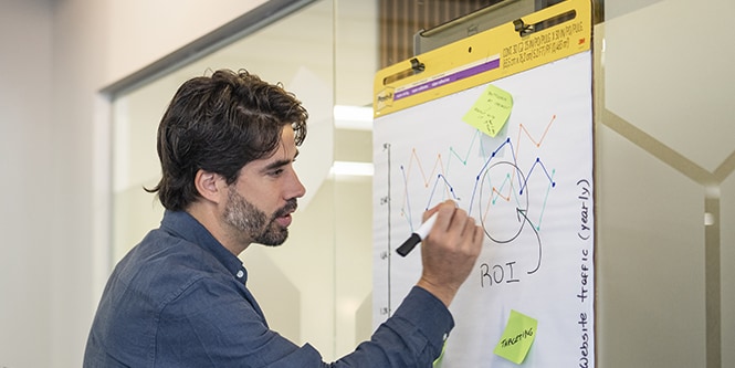 Man writing on Post-it® Meeting Chart, creating visual graphs to enhance the presentation
