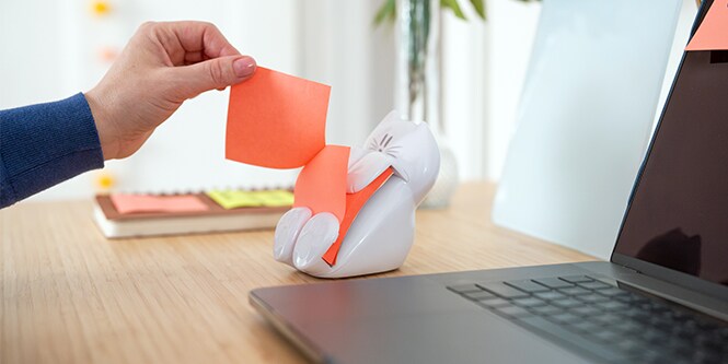 A person pulling a Post-it® Note from a white owl-shaped Post-it® Note Dispenser

