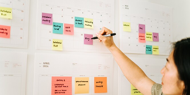 A woman planning tasks on a calendar with Post-it&reg; Notes
