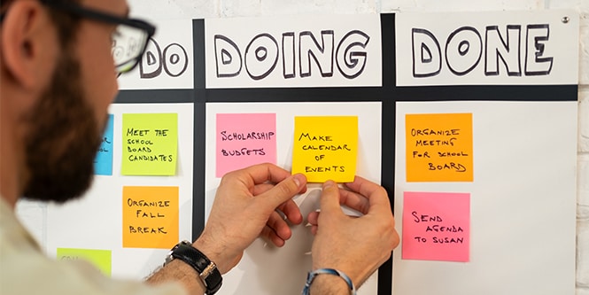 Man organising tasks on a board labelled Do Doing Done using Post-it® Notes to track progress
