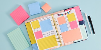 An open planner with colourful Post-it&reg; Notes, surrounded by various sizes of Post-it&reg; Notes in pink, blue, and peach

