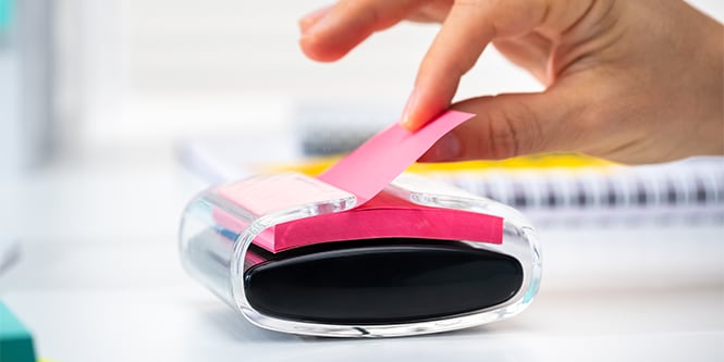 A hand pulling a pink Post-it&reg; Note from a sleek Post-it&reg; Z- Notes Dispenser
