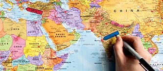 Hand marking a location on a world map with a blue marker and Post-it® Index Flags
